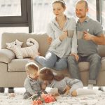 Cheerful family smiling while spending weekend together sitting parents sitting on comfortable sofa while children resting on carpet and playing