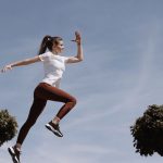 Athletic woman in action jump against a blue sky background. Captures fitness in motion.